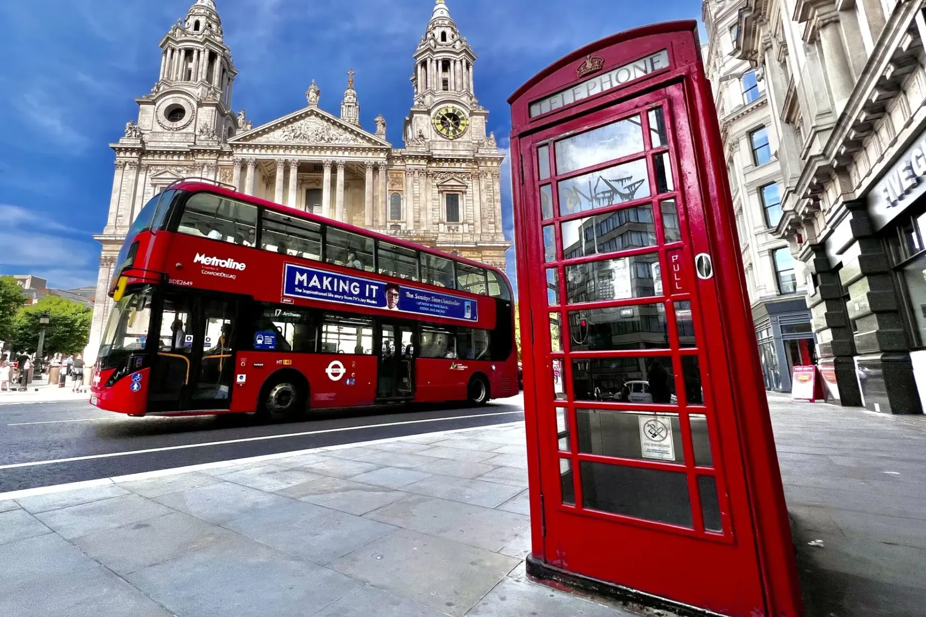 St Paul's Cathedral behind a red double-decker bus and a red telephone box on a sunny London street.