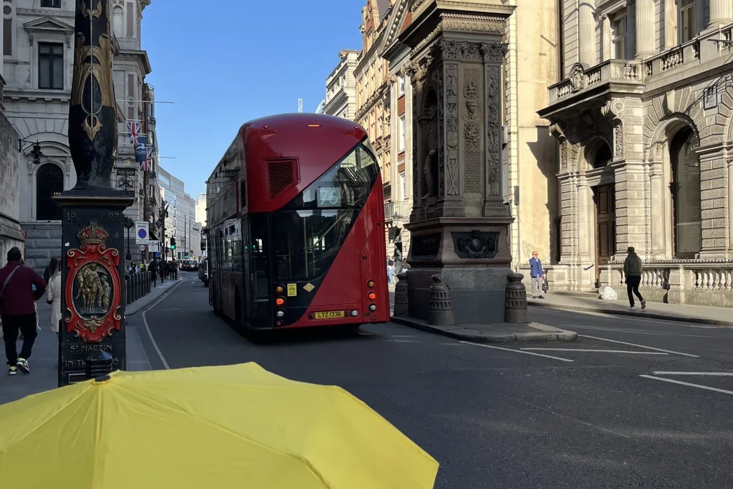 Yellow Walkative umbrella in foreground with a red double-decker bus, dragon statue, and historic buildings on a London st...