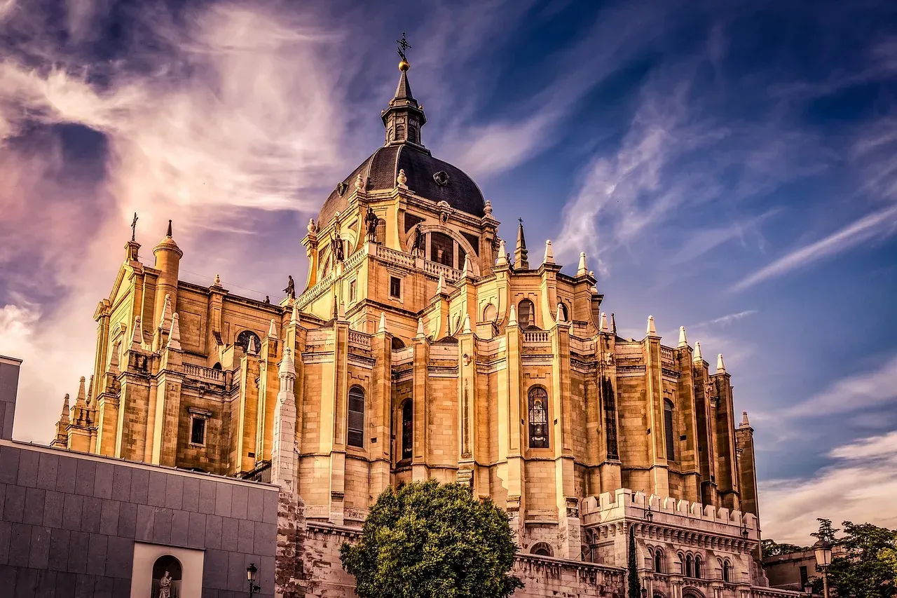 Almudena Cathedral in Madrid, with its ornate facade and dome under a dramatic sky with swirling clouds at sunset.