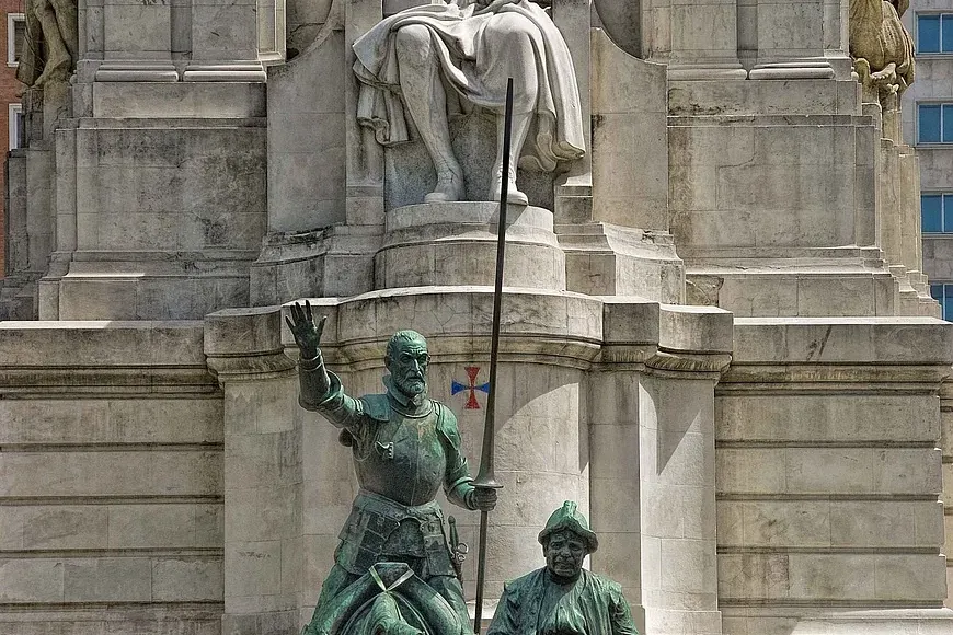 Monument with a seated stone statue of Cervantes, and bronze statues of Don Quixote on horseback and Sancho Panza on a don...