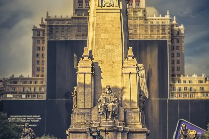 Large stone monument dedicated to Cervantes, featuring statues of Don Quixote and Sancho Panza on horseback, with a buildi...