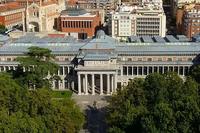Aerial view of the Museo del Prado in Madrid, a grand Neoclassical building with a portico of columns, surrounded by green...
