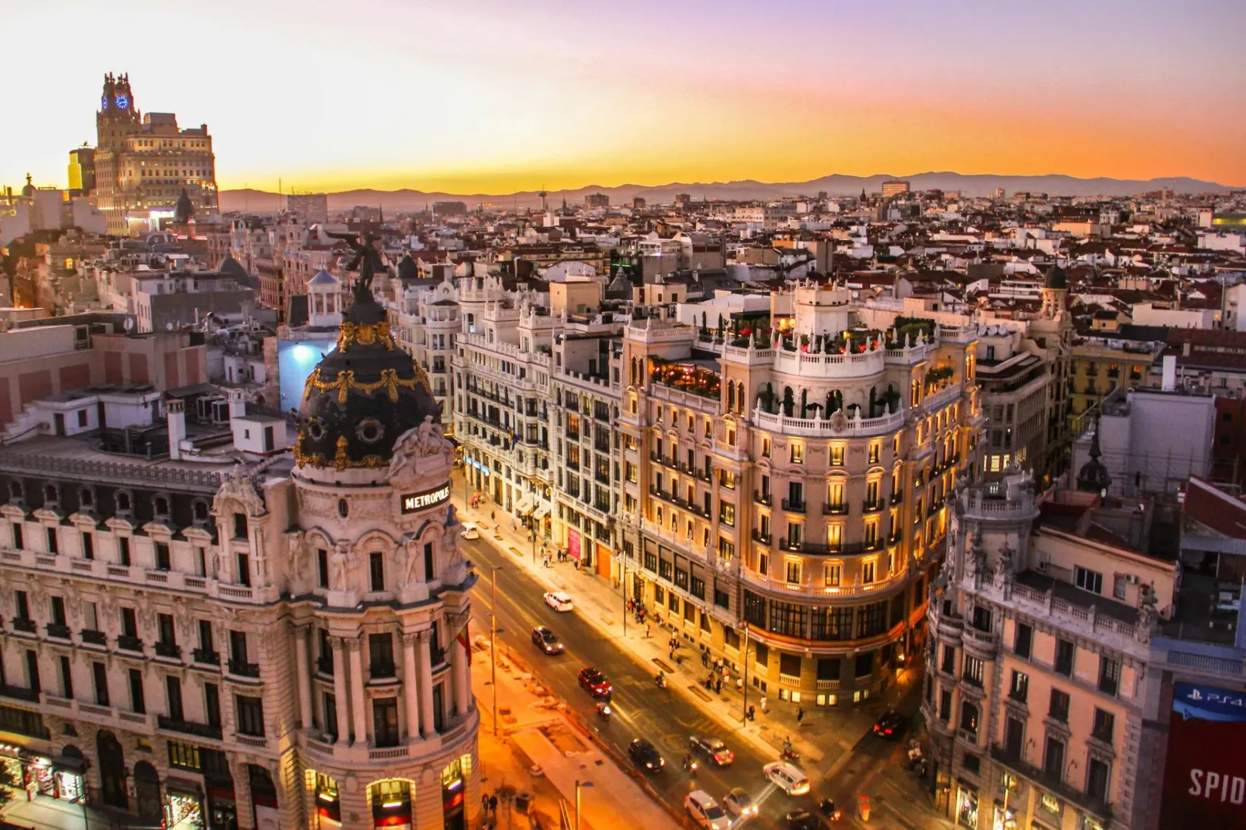 Aerial view of Madrid city at sunset. The ornate Metrópolis Building with its dome is prominent, with cars and pedestrians...