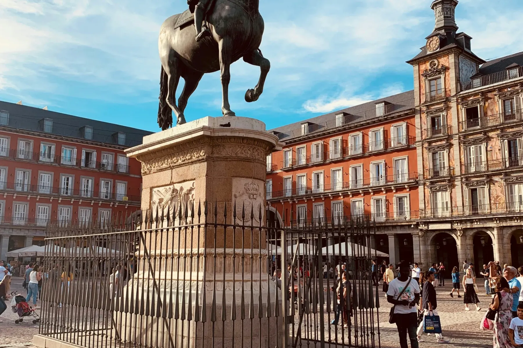 Bronze equestrian statue of King Philip III on a stone pedestal in a historic city square with red buildings and people.