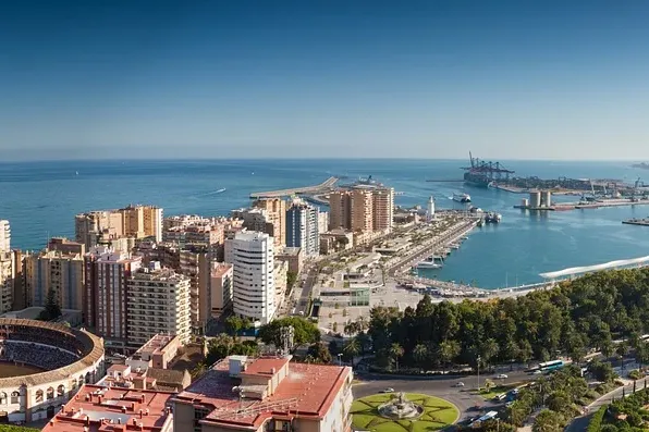 Panoramic view of Malaga cityscape with La Malagueta bullring, the port, and the Mediterranean Sea under a blue sky.