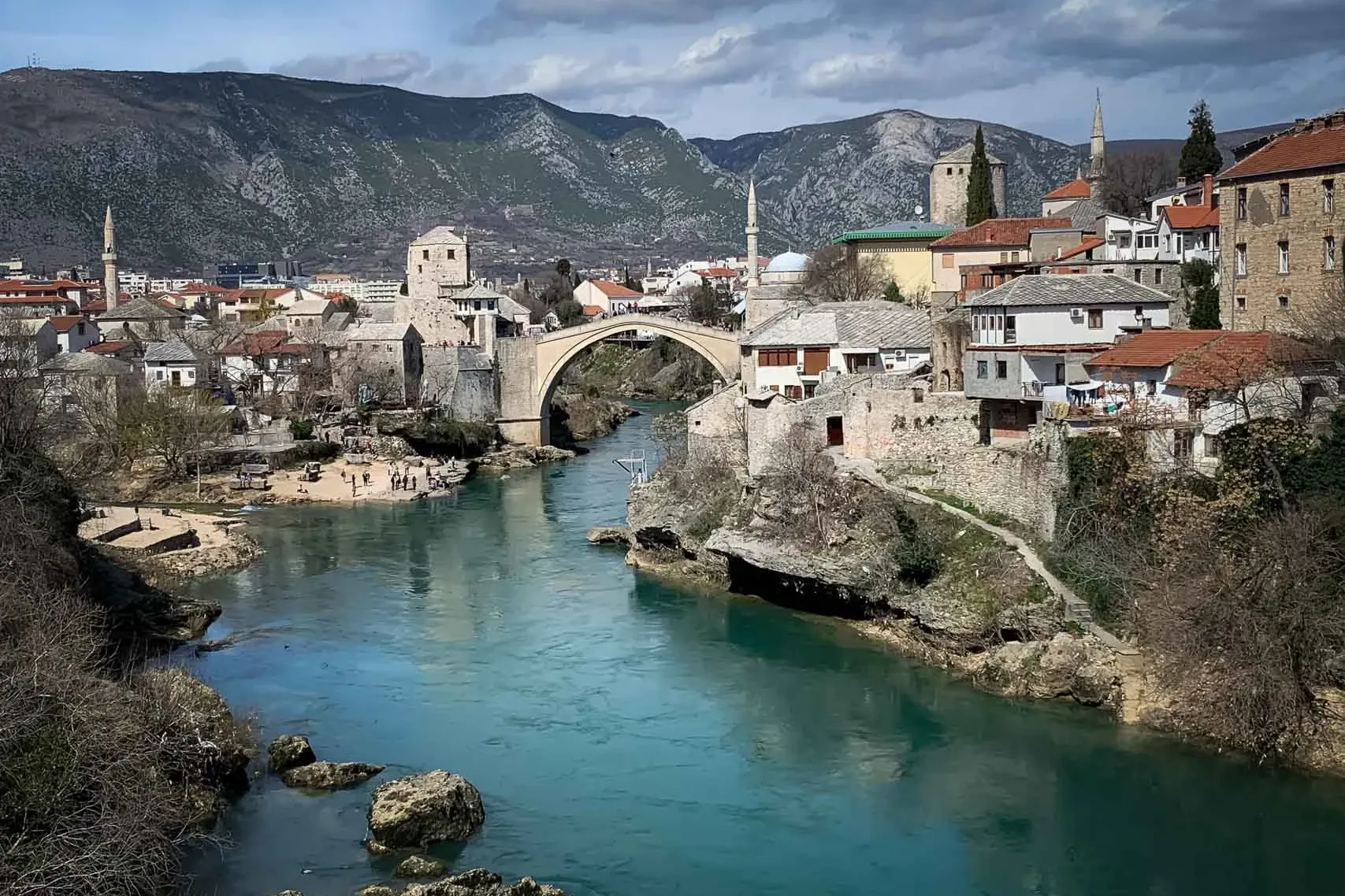 Stari Most, a historic stone arch bridge, spans the turquoise Neretva River in Mostar, flanked by traditional buildings an...