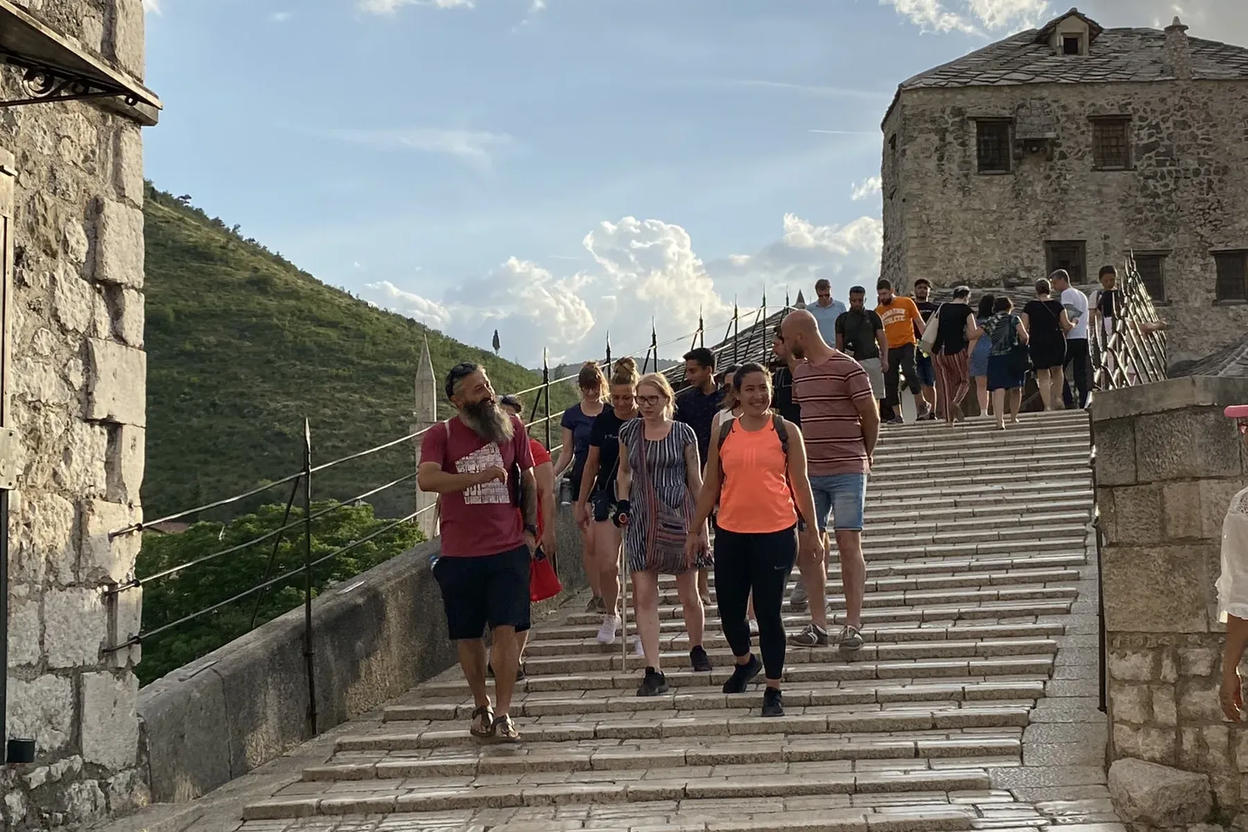 Group of tourists and a guide walking down ancient stone steps next to a historic stone building and green hillside in Mos...