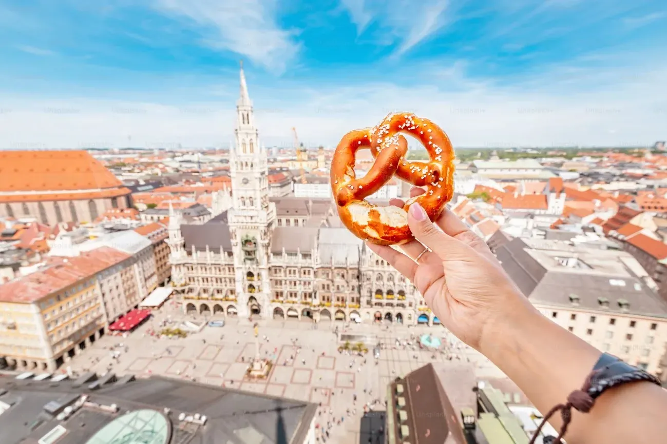 A pretzel held against the backdrop of Munich's Marienplatz.