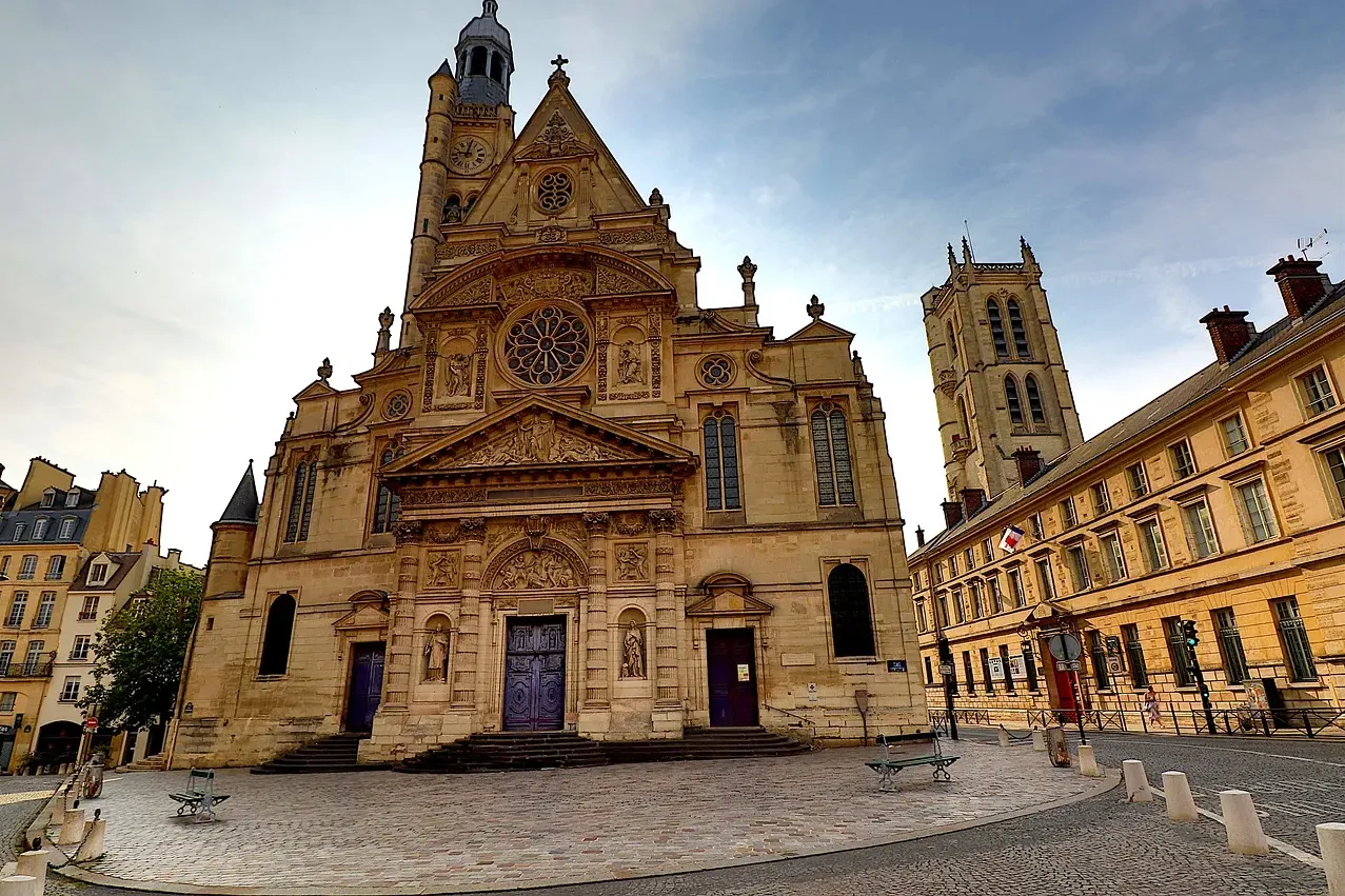 The ornate facade of Saint-Étienne-du-Mont church in Paris, with a clock tower and stained-glass windows, under a partly c...