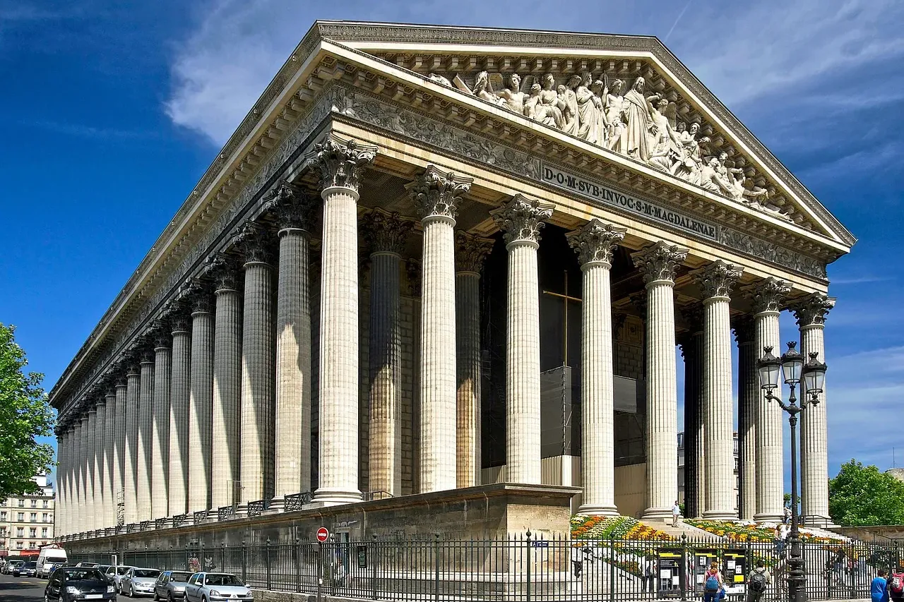 Grand neoclassical church with a long row of Corinthian columns, a detailed pediment sculpture, and steps leading to the e...