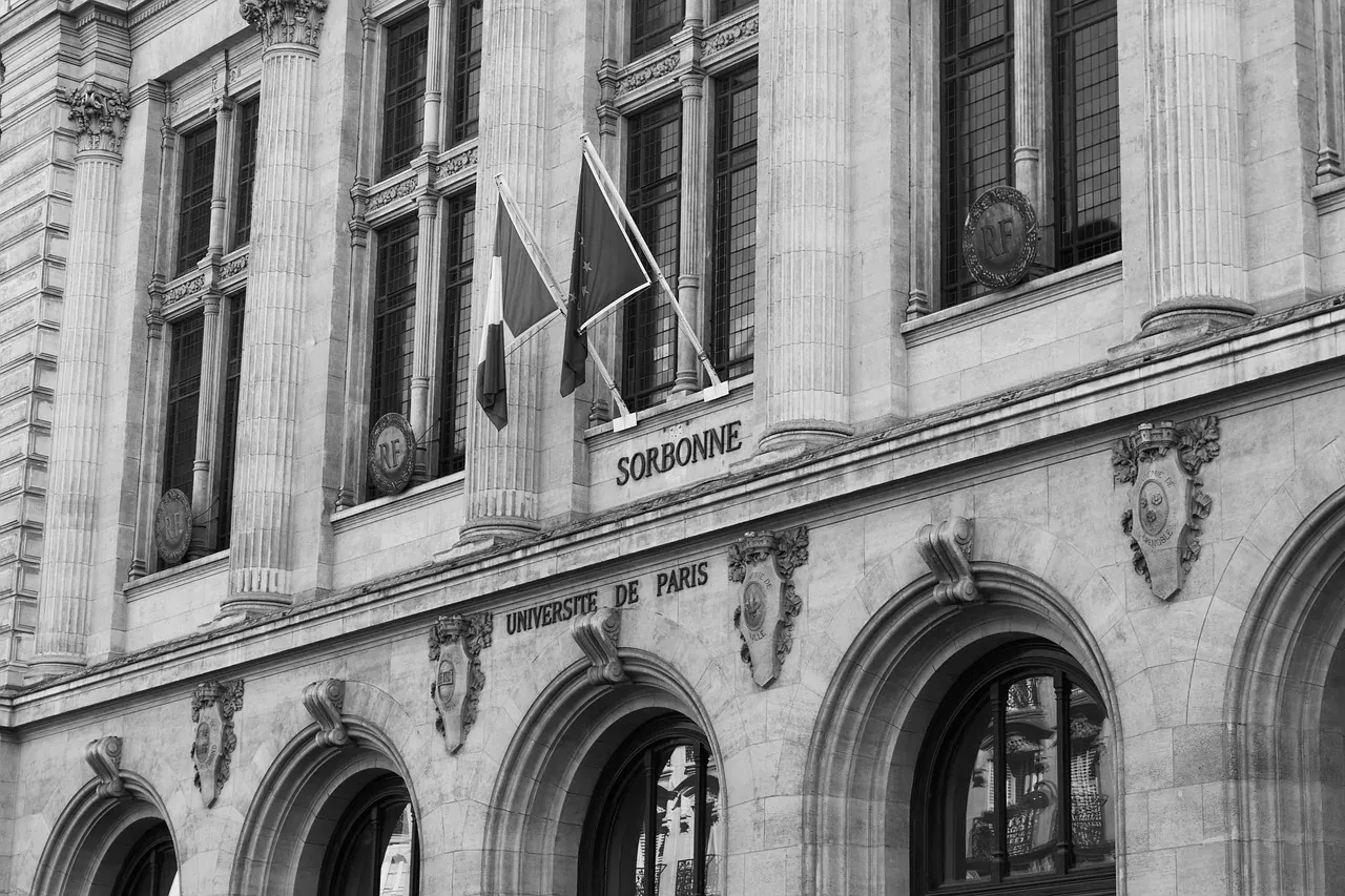 Black and white detailed view of the Sorbonne University facade in Paris, with columns, arched windows, and flags.