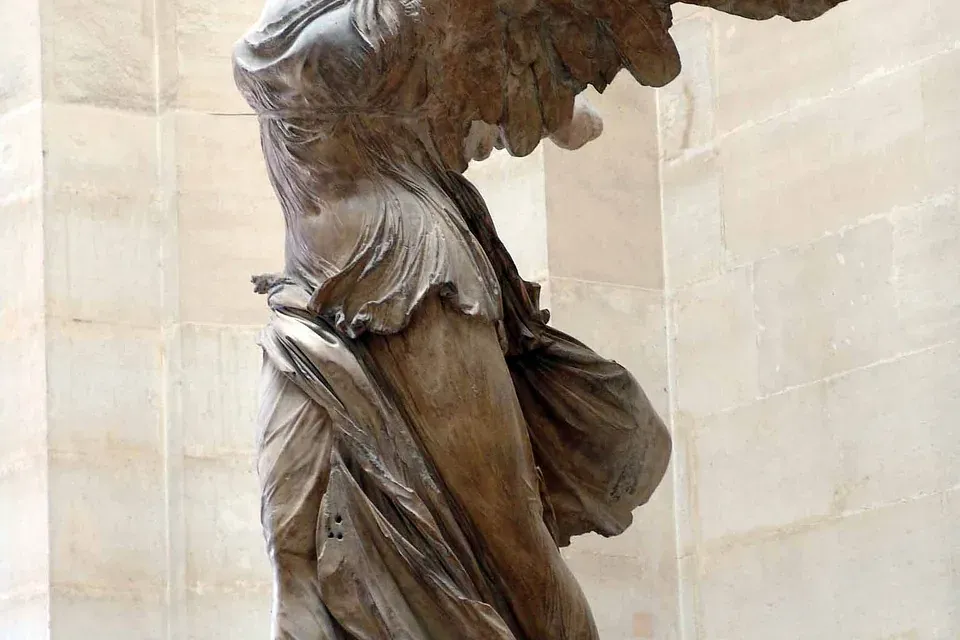 Large marble statue of the Winged Victory of Samothrace, headless and armless, draped in flowing fabric, on a pedestal.