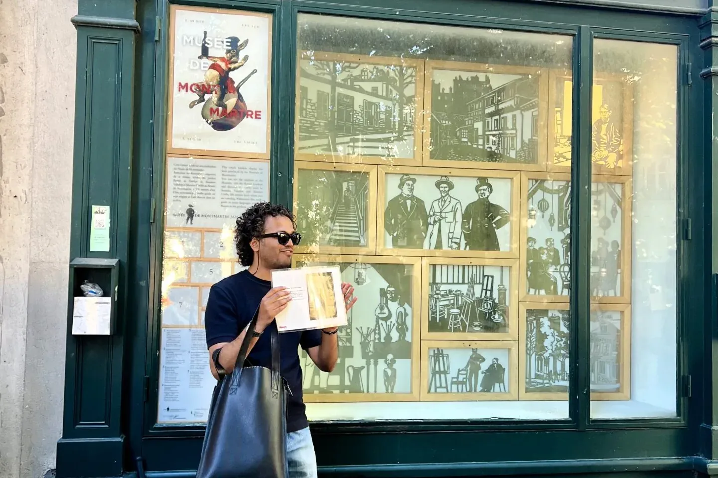 Man in sunglasses with a book, standing before the Le Bateau-Lavoir building with historical Montmartre illustrations in i...