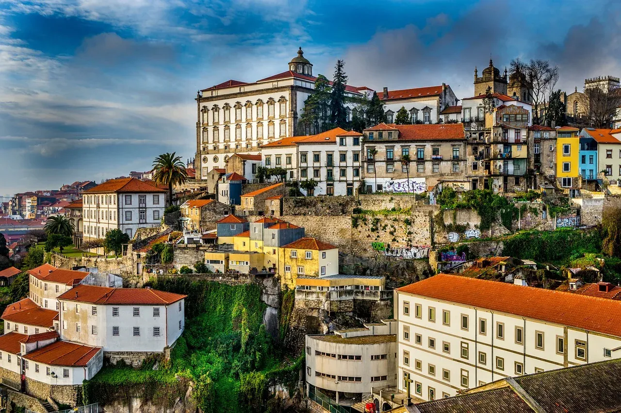 Historic Porto cityscape with traditional buildings, red tiled roofs, and a large white palace-like building on a hill. Gr...