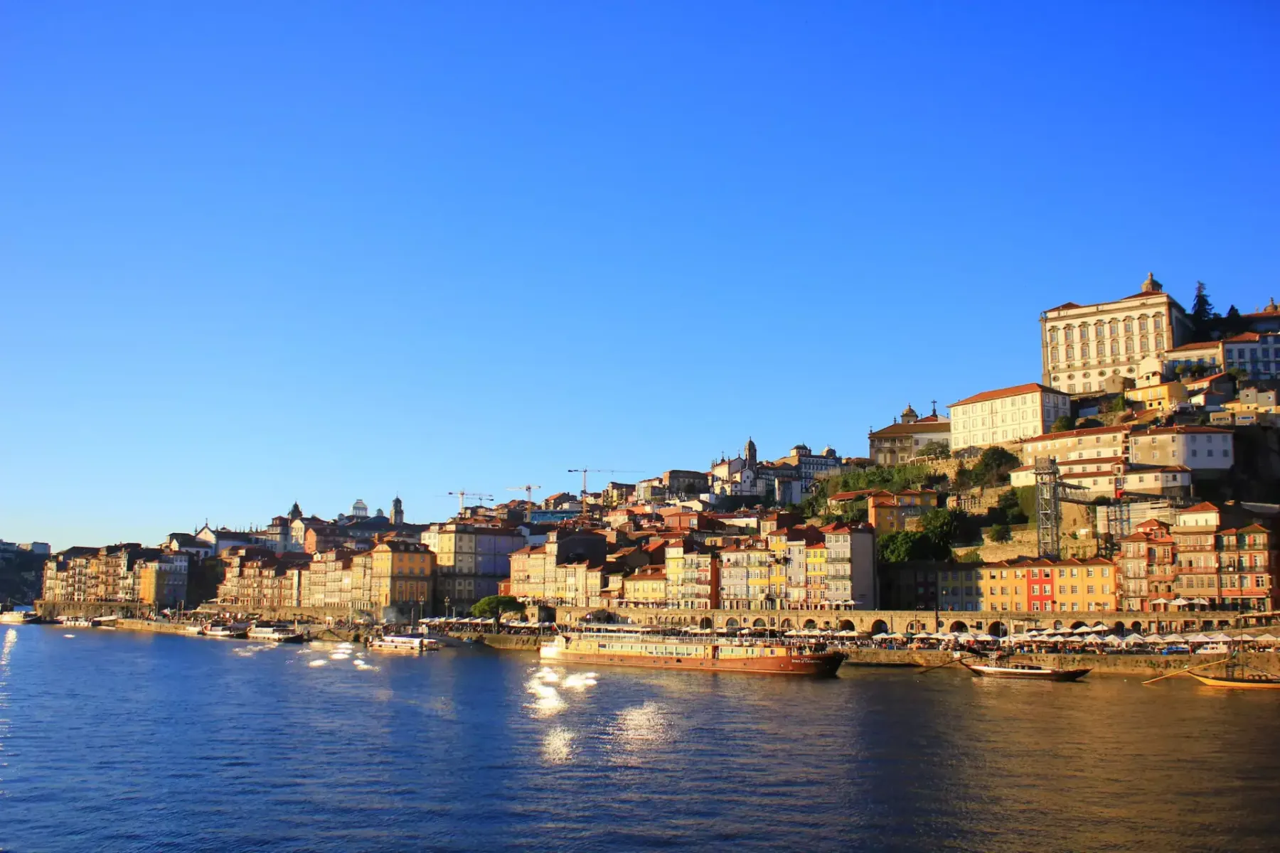 Porto's Ribeira district with colorful buildings cascading down a hill towards the Douro River, boats docked along the wat...