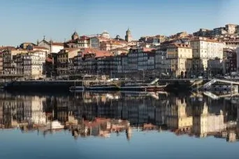 Colorful historic buildings of Porto's Ribeira district line the Douro River, reflecting in its calm waters under a clear ...