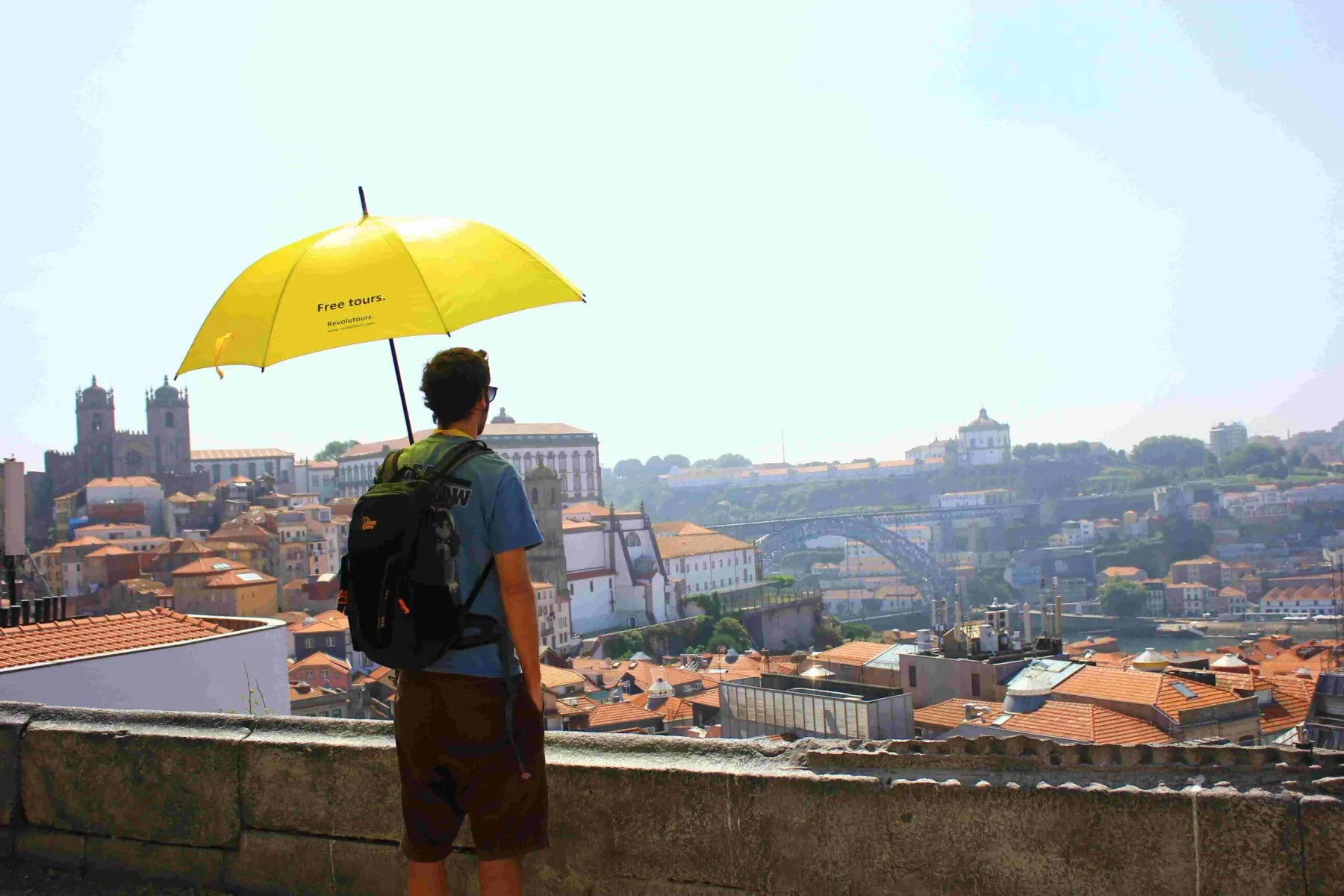 Back of a person with a yellow umbrella, overlooking Porto's skyline including Dom Luís I Bridge and cathedral towers.
