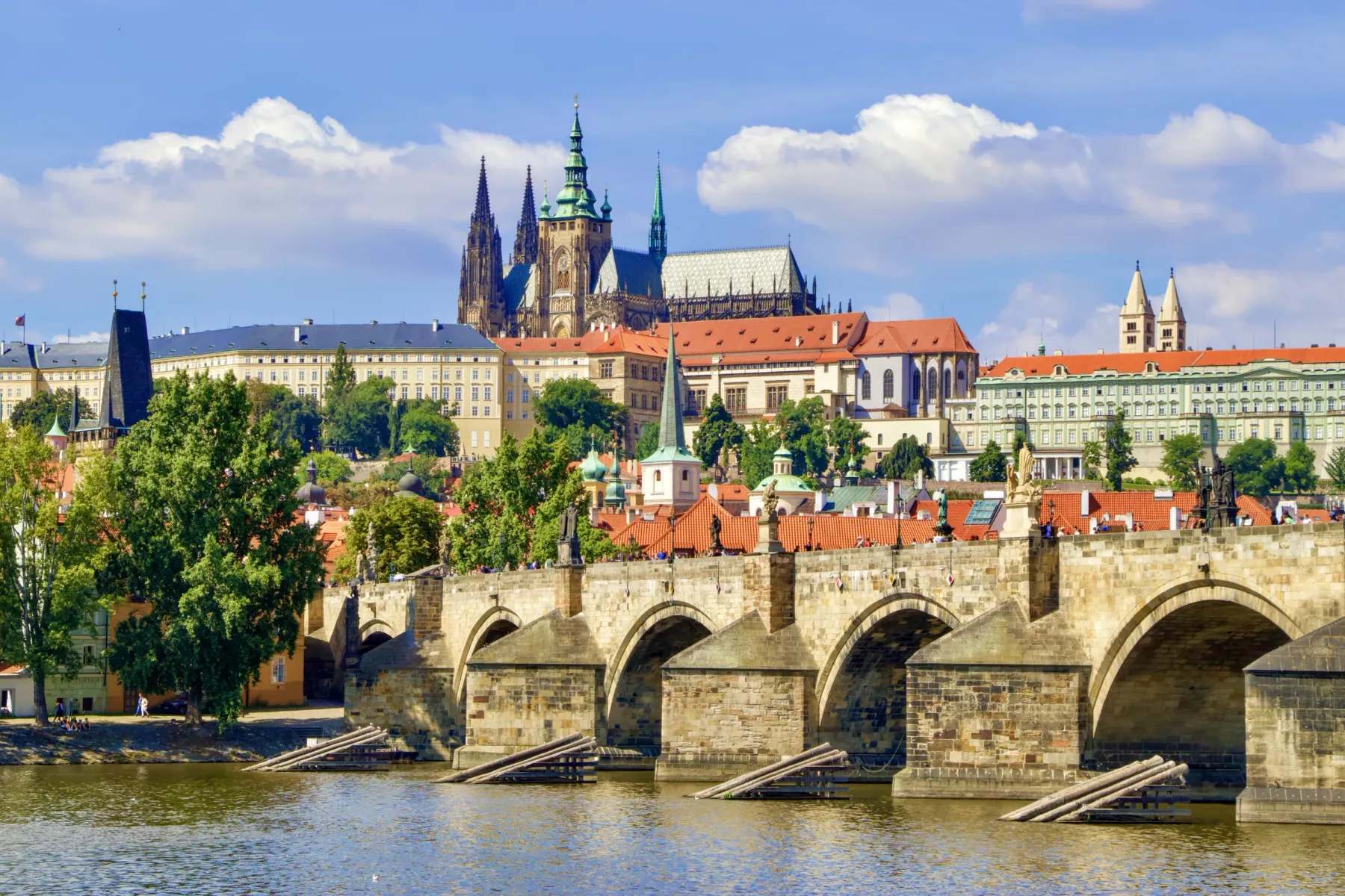 View of Charles Bridge with statues over Vltava River, with Prague Castle and St. Vitus Cathedral on a hill under a cloudy...