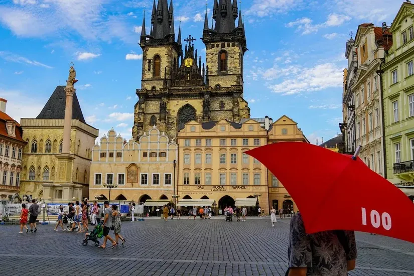 Church of Our Lady before Týn towers over Prague's Old Town Square, with historic buildings and people walking.