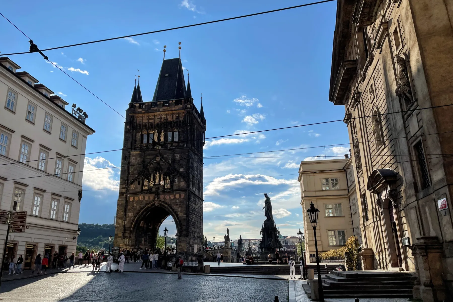 View of the Lesser Town Bridge Tower and statues of Charles Bridge in Prague, with historic buildings and a cobblestone st...