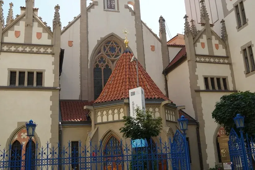 Exterior view of the Pinkas Synagogue in Prague with a golden Star of David on its roof and a blue ornate fence in front.