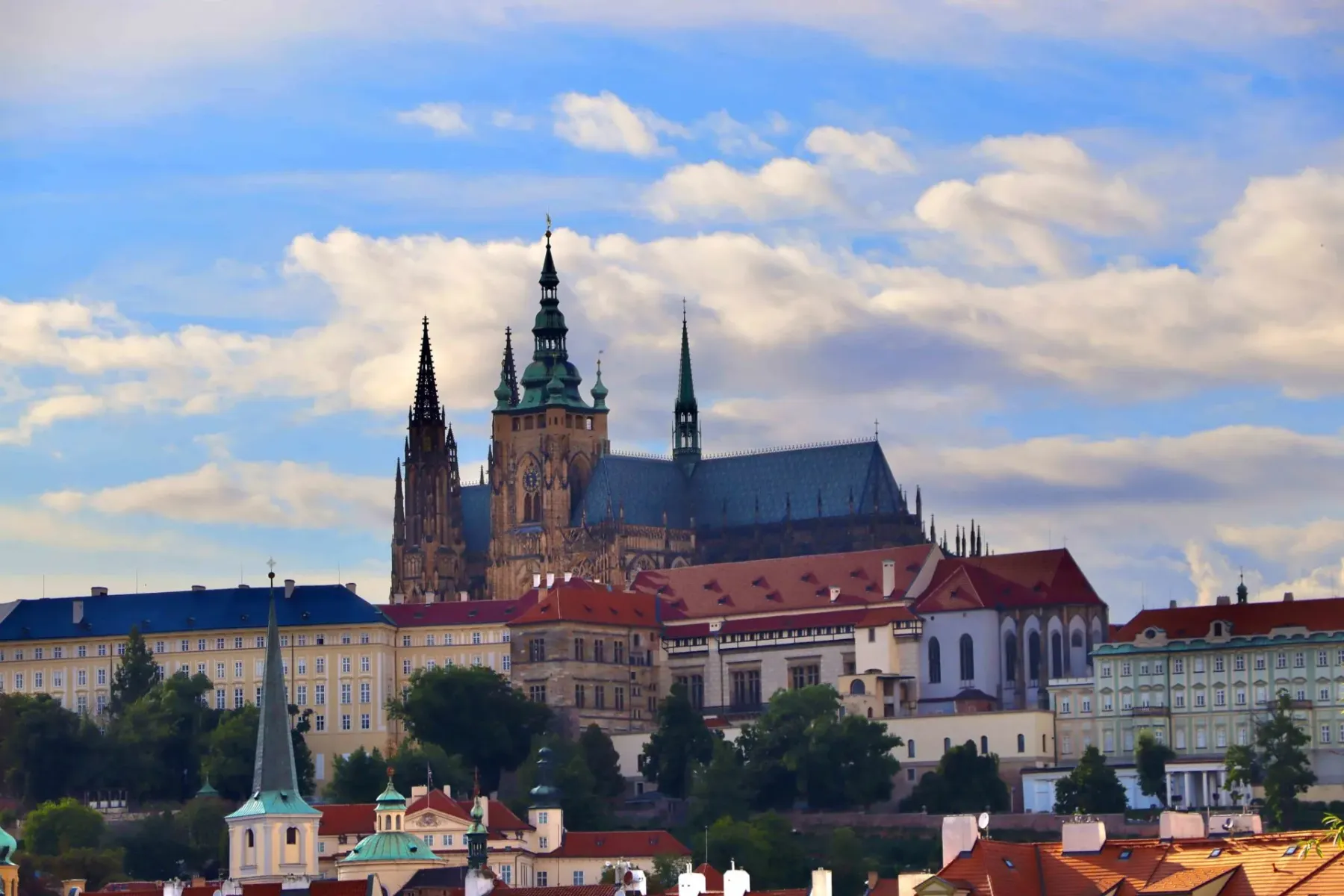 St. Vitus Cathedral and Prague Castle complex visible above various city buildings under a partly cloudy sky.