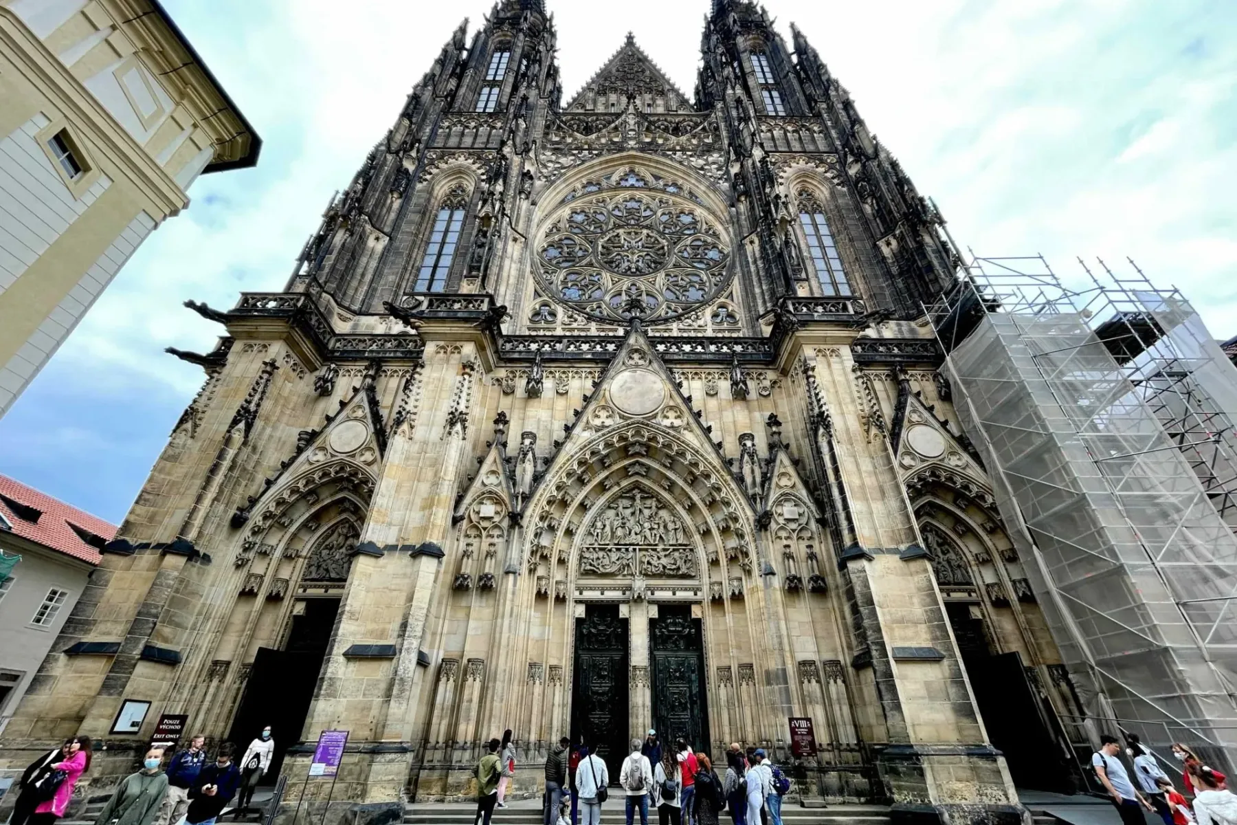 Front facade of St. Vitus Cathedral in Prague, showcasing Gothic architecture, a large rose window, twin spires, and peopl...