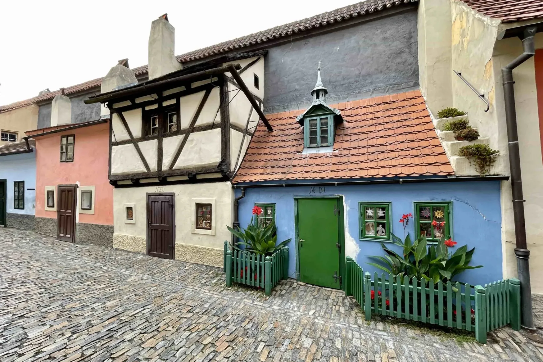 Colorful historic houses with tiled roofs lining a narrow cobblestone street, including a blue house with green door and w...