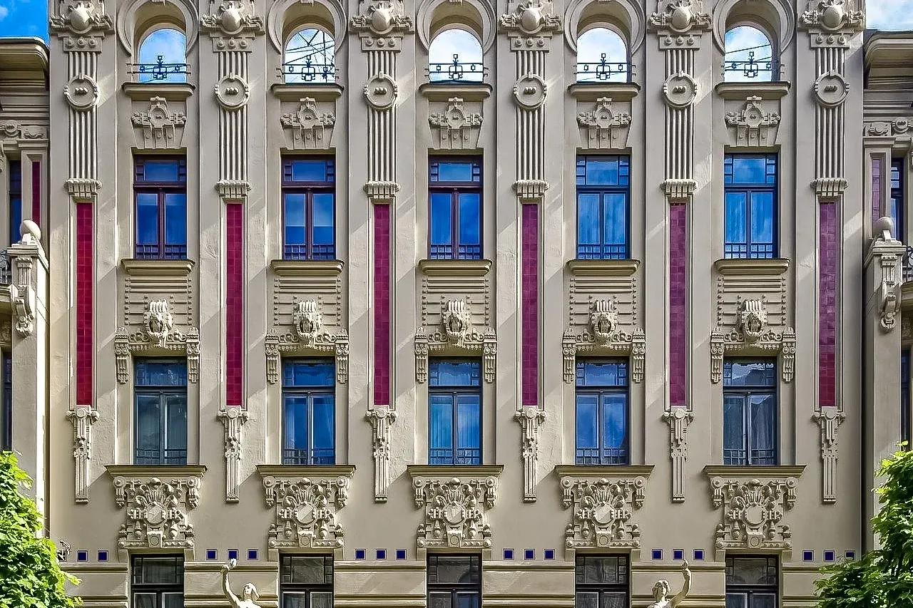 Elaborate Art Nouveau building facade in Riga with detailed sculptures, ornate windows, vertical red accents, and two stat...