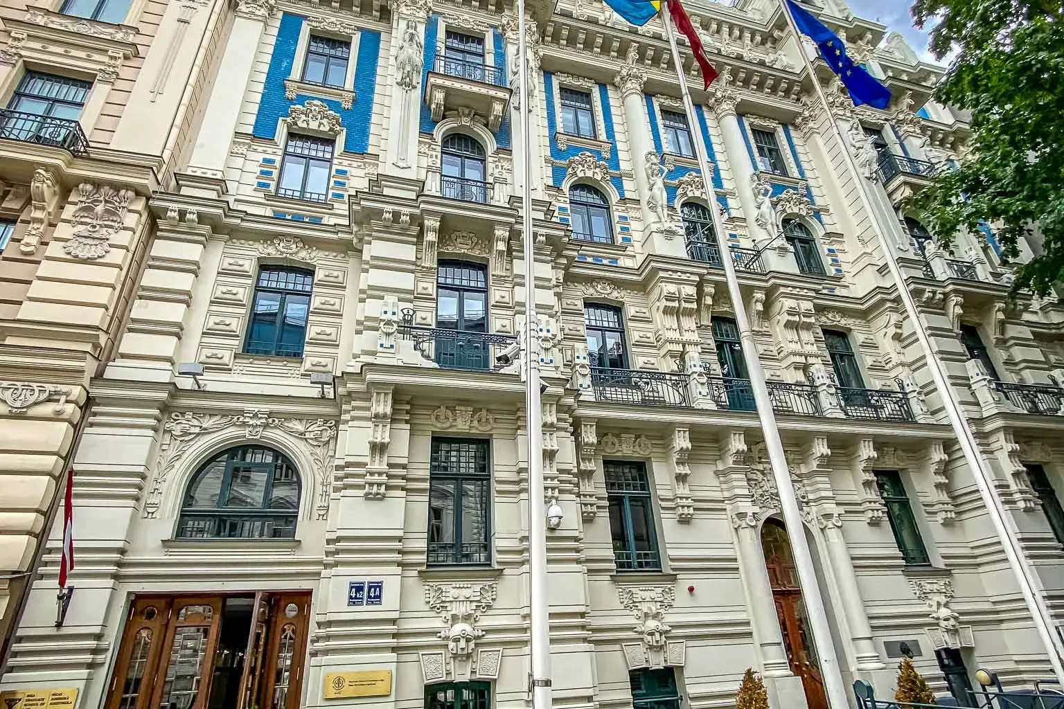 Ornate Art Nouveau building in Riga with cream facade, blue details, dark windows, and flags of Sweden and the EU.