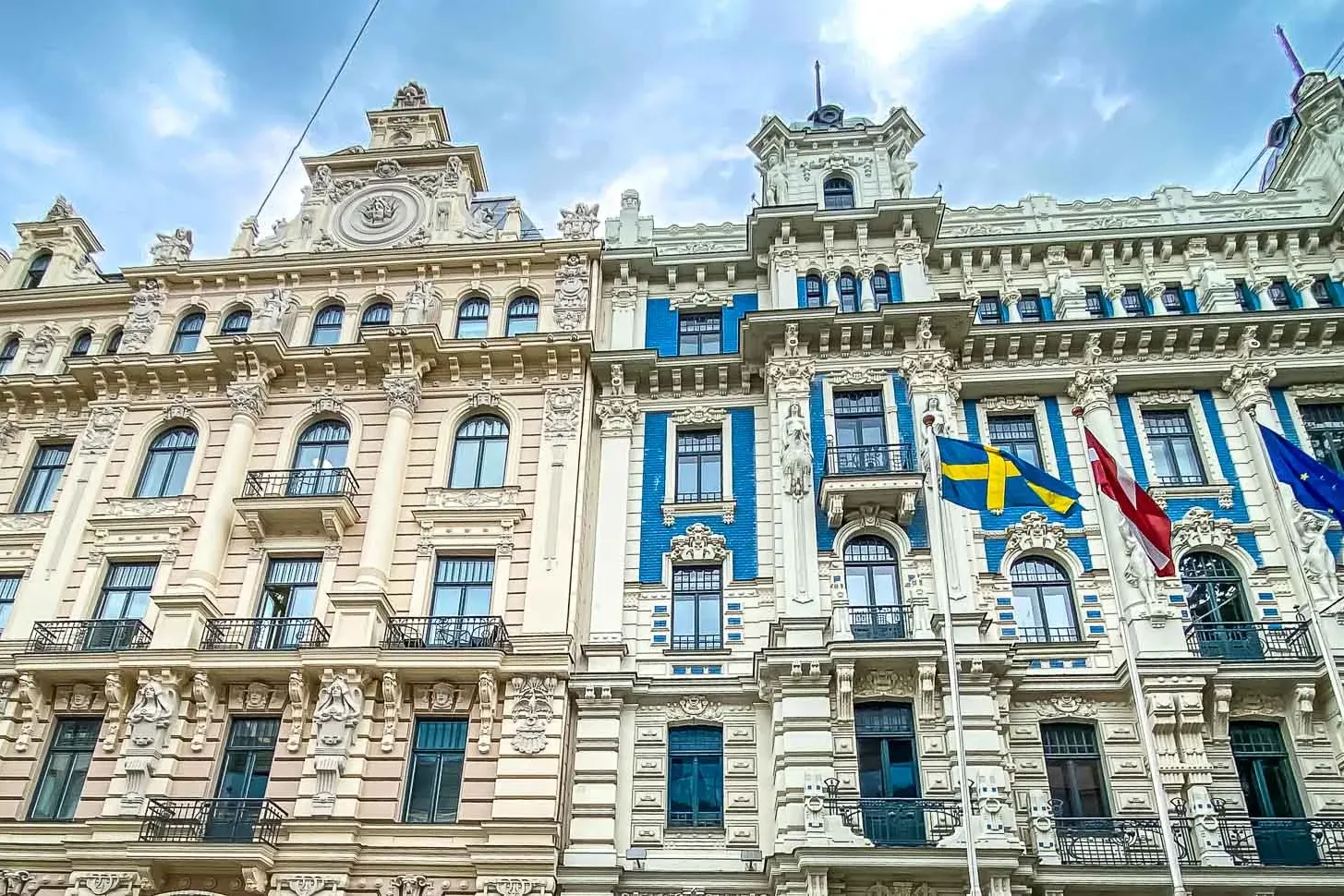 Ornate Art Nouveau buildings in Riga with detailed facades, balconies, and flags of Latvia, Sweden, and the EU.