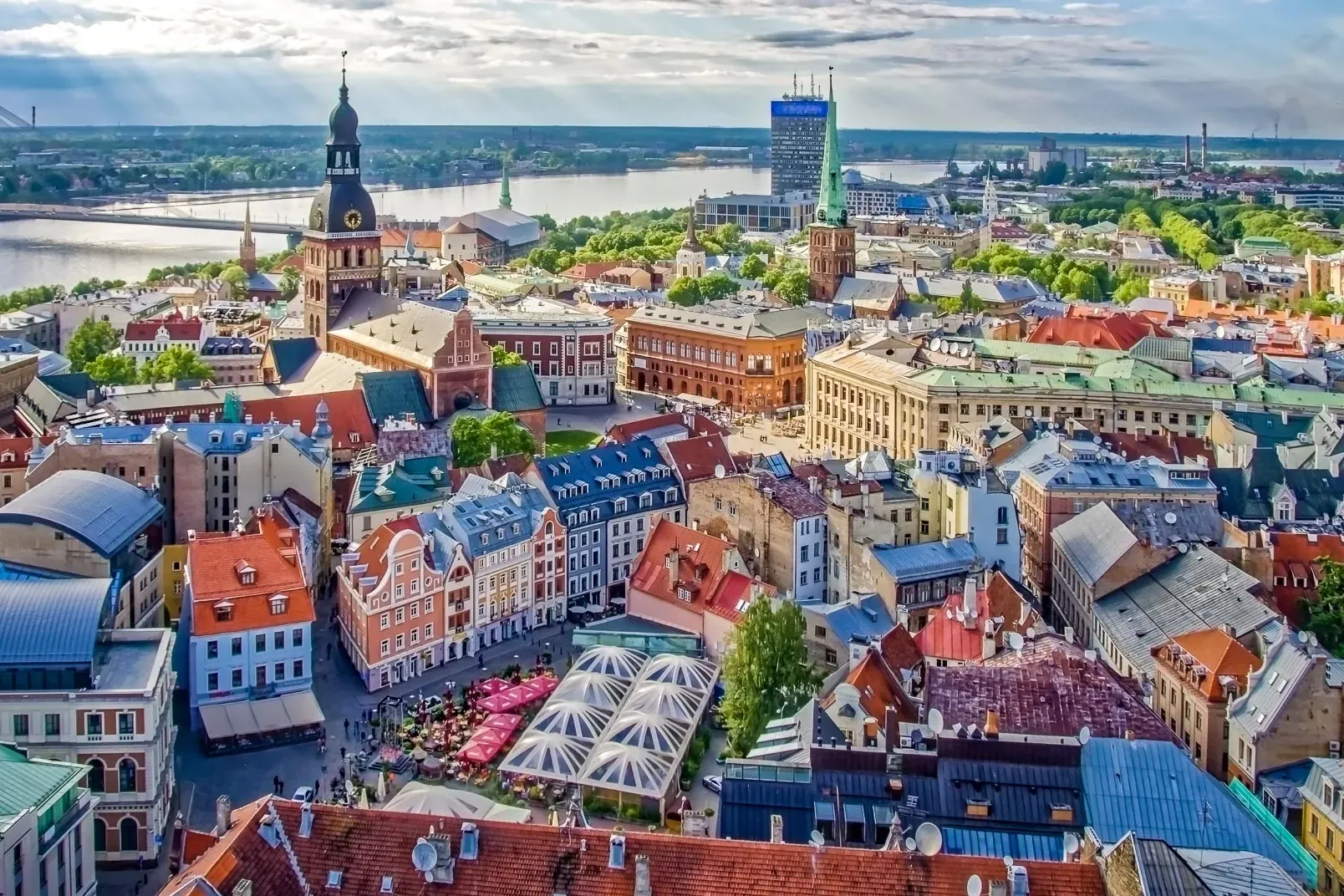 Aerial view of Riga Old Town with colorful buildings, St. Peter's Church spire, Daugava River, and Vansu Bridge under a cl...