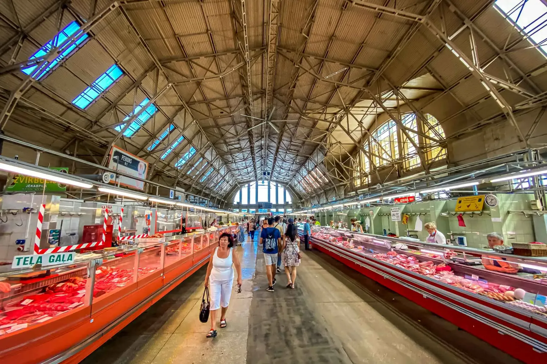 Interior of Riga Central Market meat pavilion, with long refrigerated display counters filled with fresh meat and shoppers.
