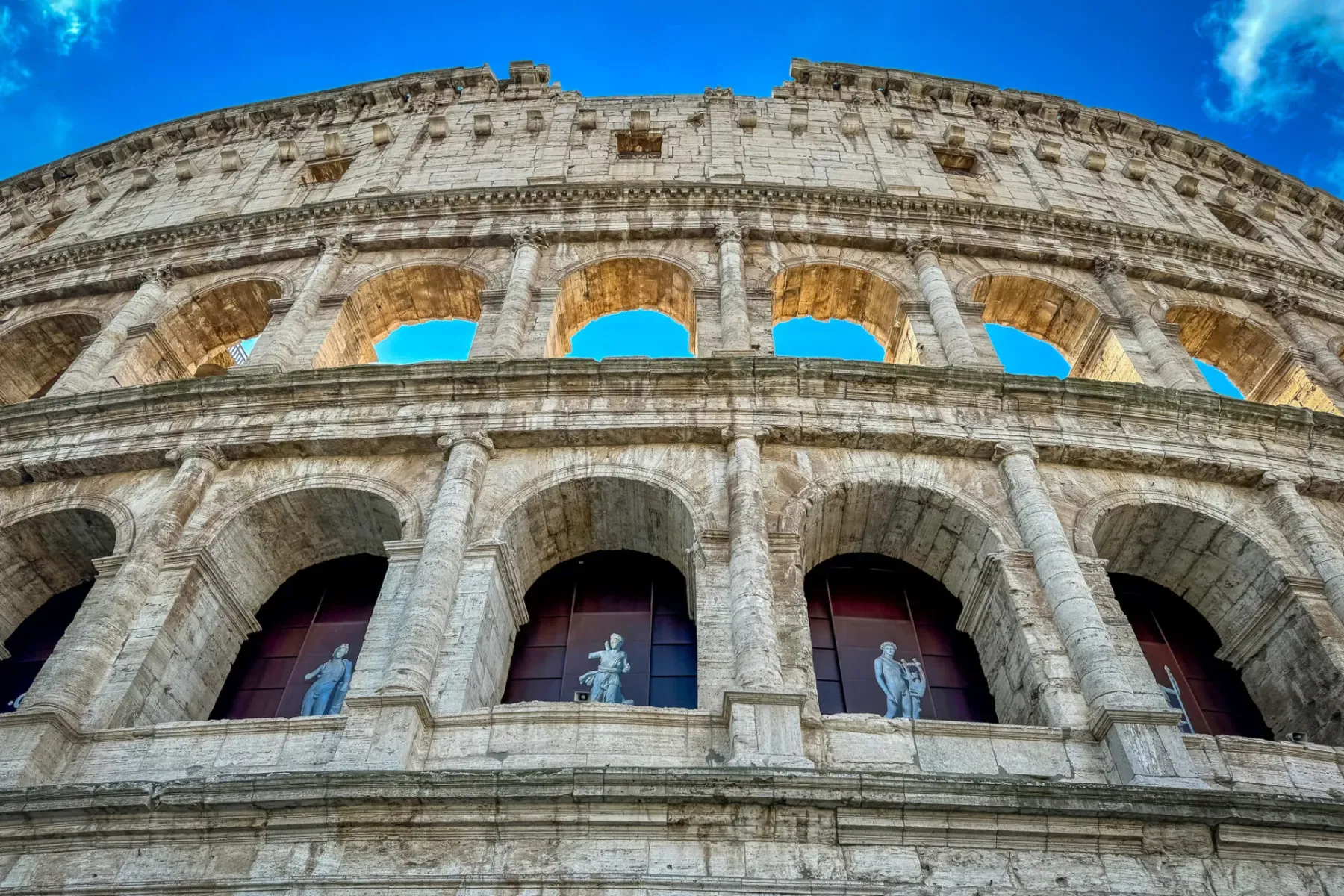 Low-angle view of the Colosseum in Rome, showcasing its impressive architecture and statues.