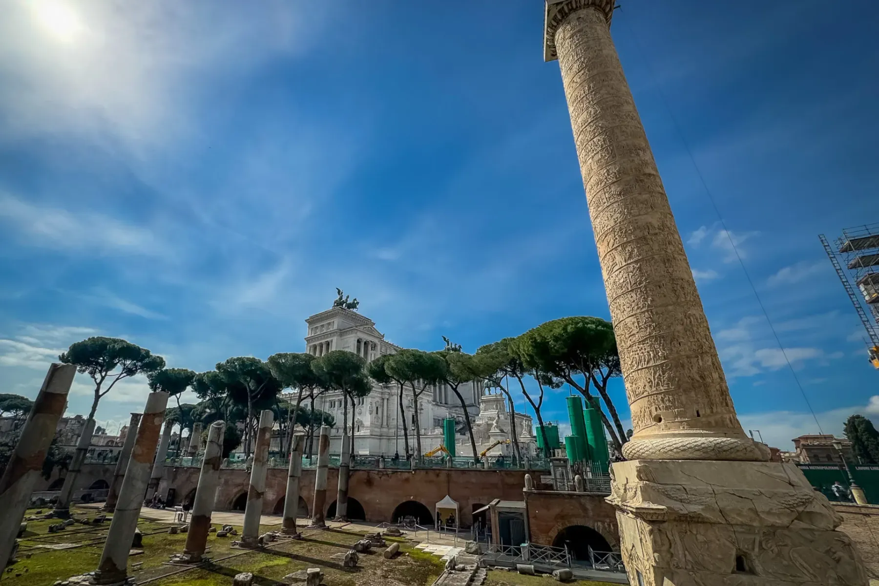 Trajan's Column with intricate carvings, ancient Roman ruins in the foreground, and the Altare della Patria in the backgro...