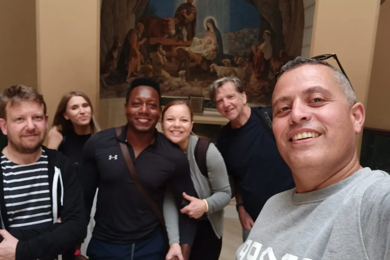 Happy tourists on a guided tour in Rome, posing for a selfie in front of a Nativity painting.