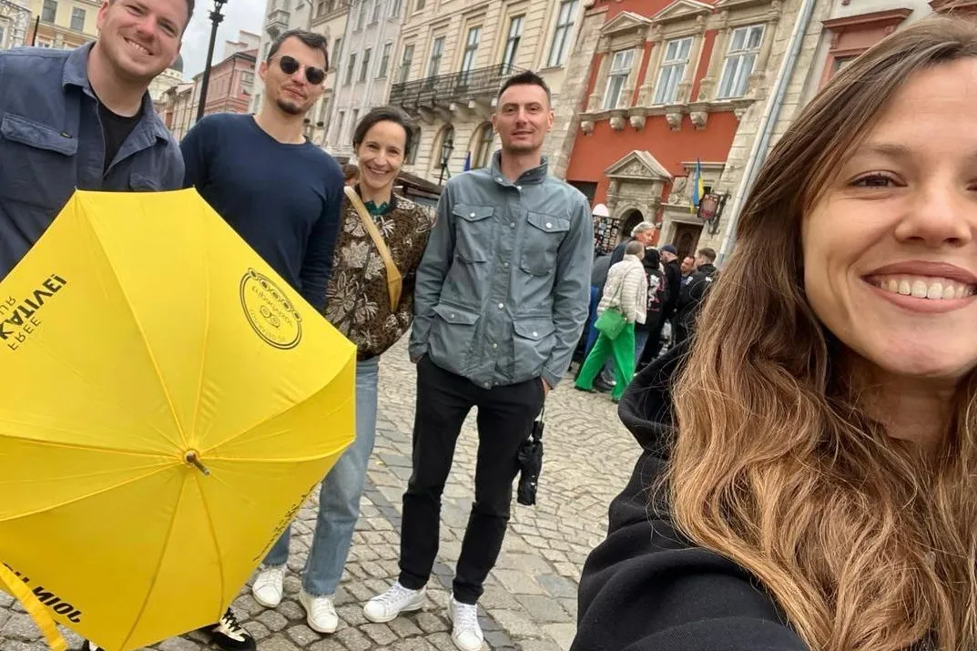 Group of five people, including a guide with a yellow Walkative umbrella, on a cobblestone street in Lviv's Old Town.
