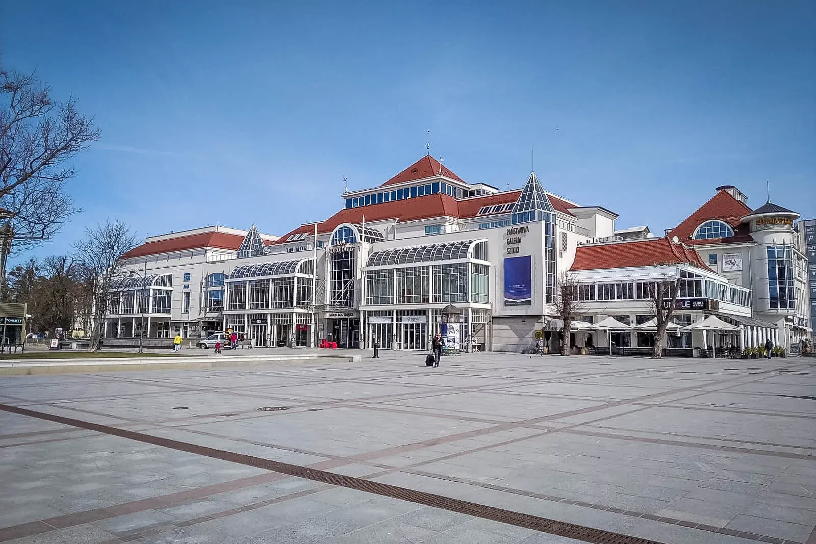 The Grand Hotel building and State Art Gallery on a wide paved plaza in Sopot, under a clear blue sky.