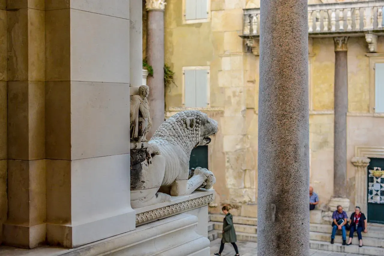 Carved stone lion statue on a pedestal, partially obscured by a column, within an ancient palace setting in Split.