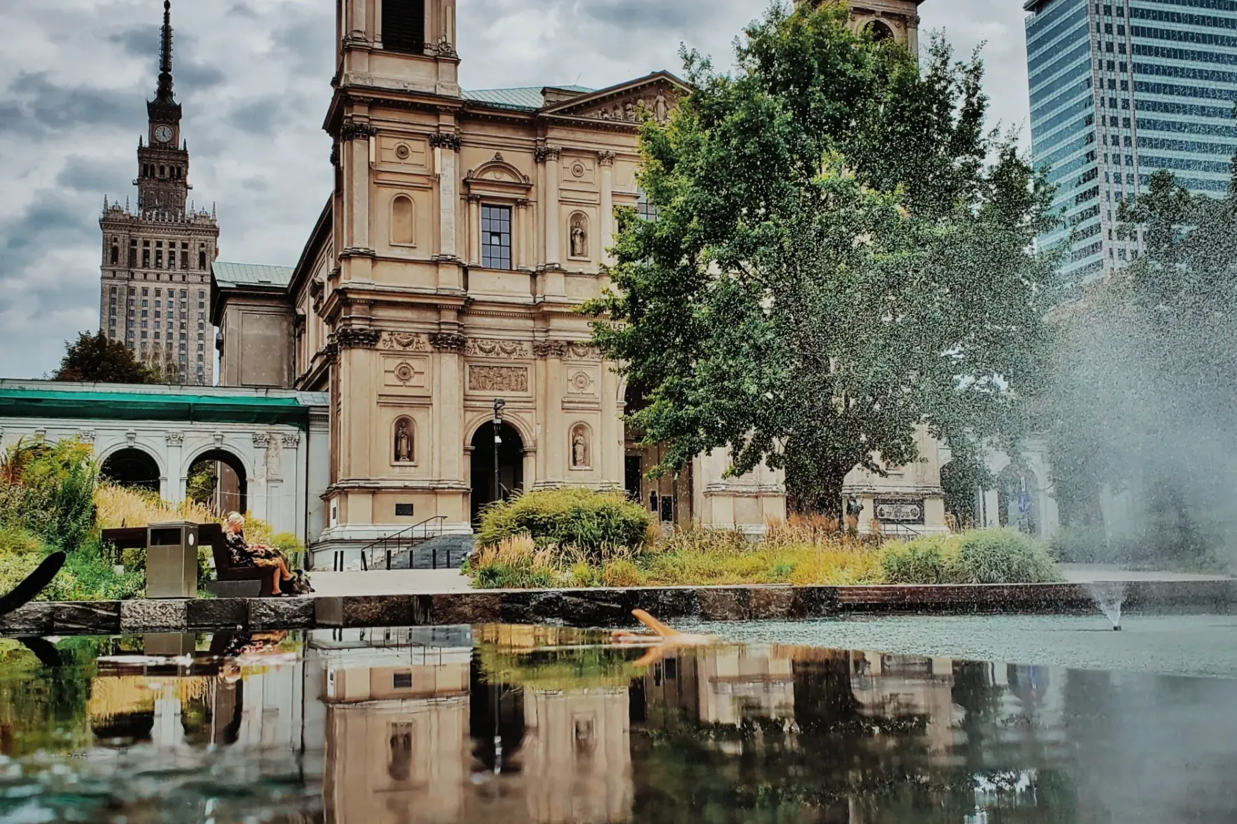 St. Alexander's Church with its two towers and green spires reflected in water. The Palace of Culture and Science and a mo...