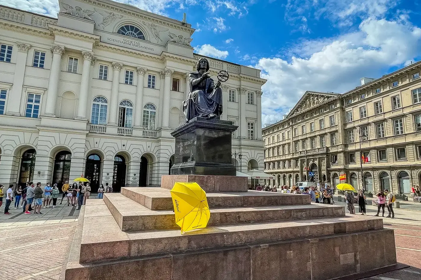 Bronze statue of Nicolaus Copernicus with an armillary sphere in Warsaw, in front of the Staszic Palace under a blue sky.