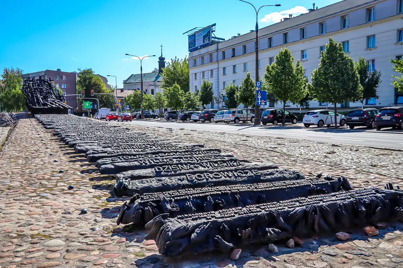 Monument to the Fallen and Murdered in the East in Warsaw, with dark, sculpted forms resembling railway sleepers on cobble...