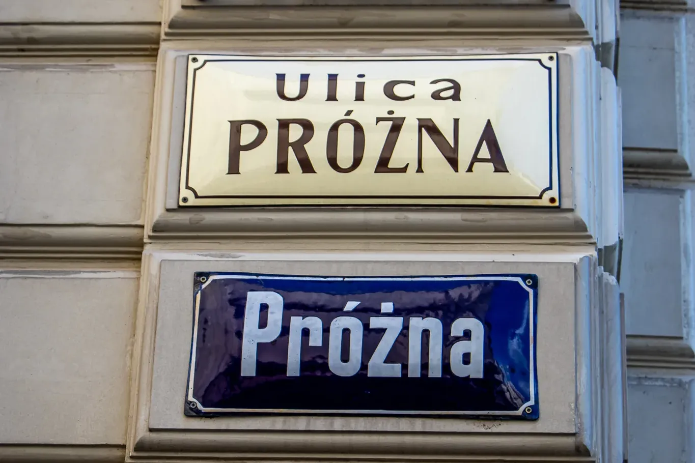 Stack of four historic and modern street signs for Ulica Próżna, including one with Cyrillic script, on a Warsaw building ...