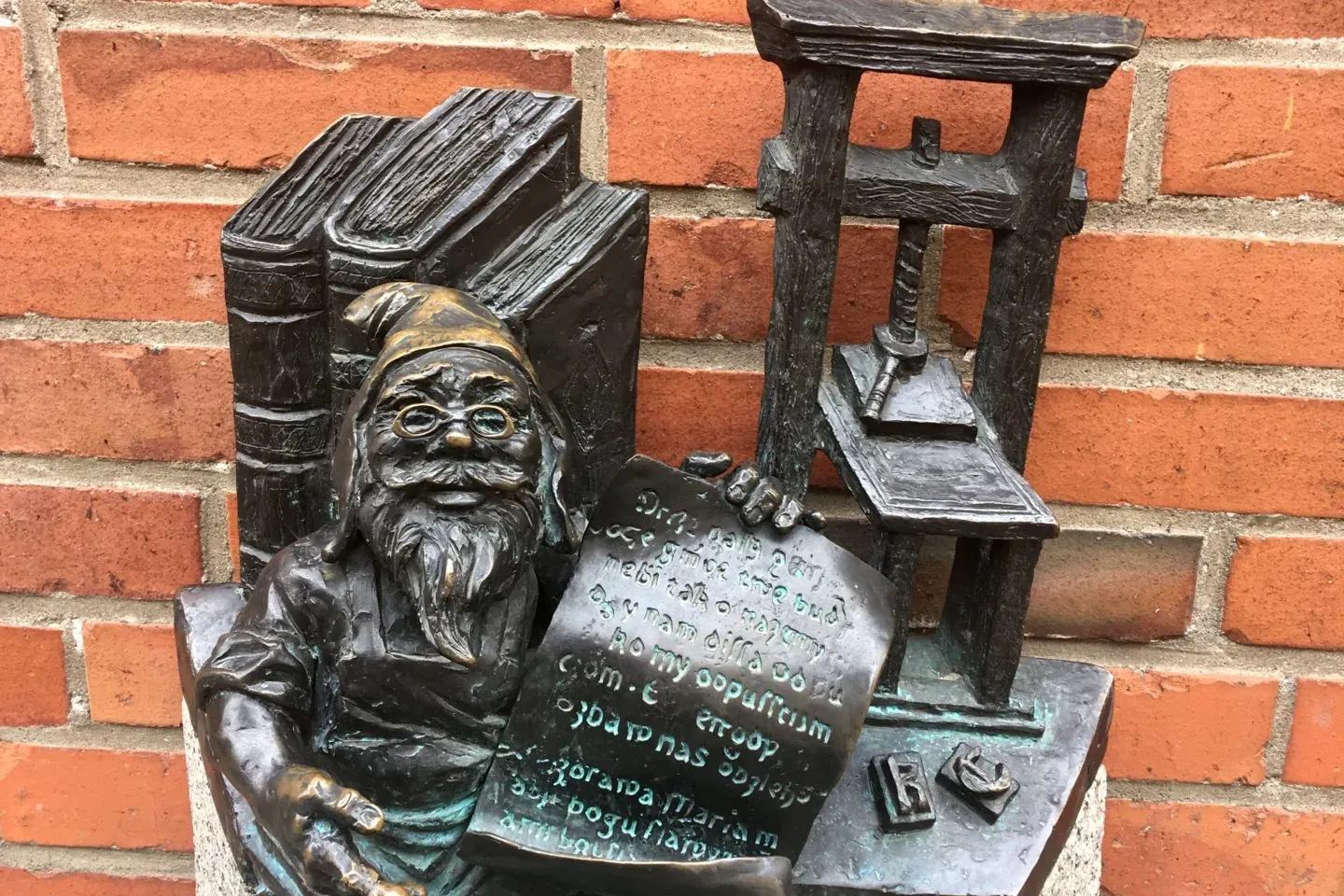 Bronze dwarf statue in Wrocław, Poland, sitting by a printing press and books.