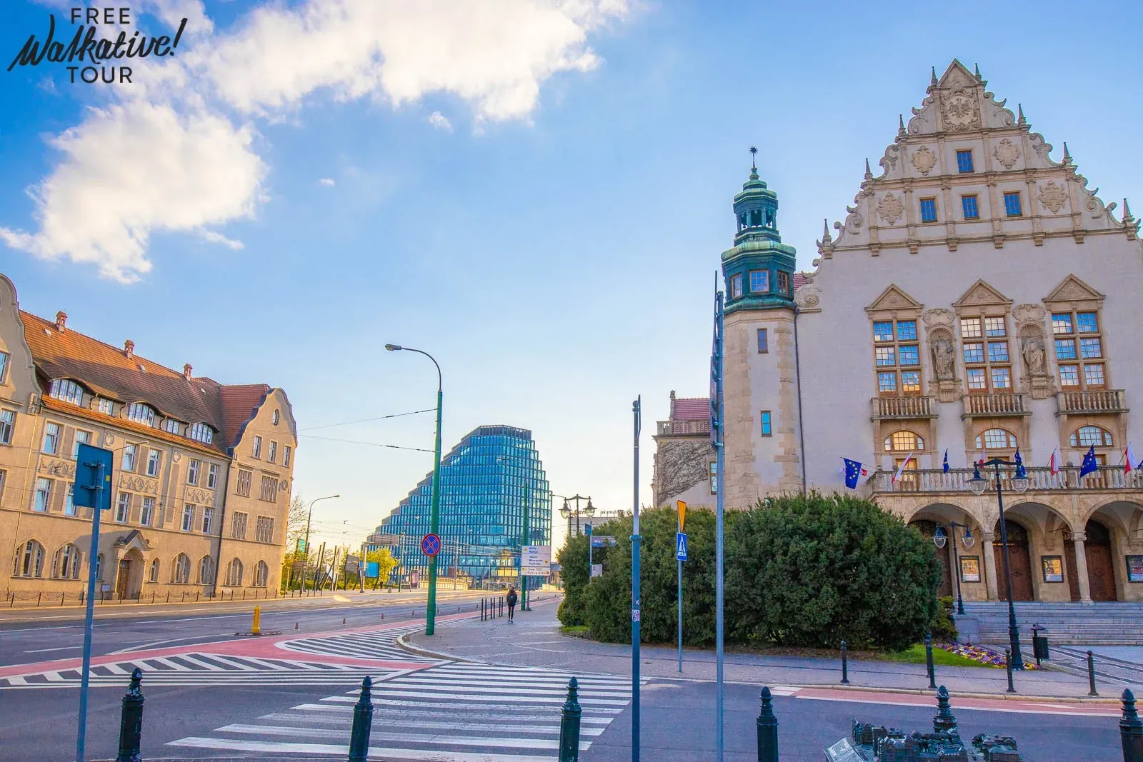 Street intersection in Poznan with the historic Collegium Minus building and a modern glass Baltyk Tower under a blue sky.