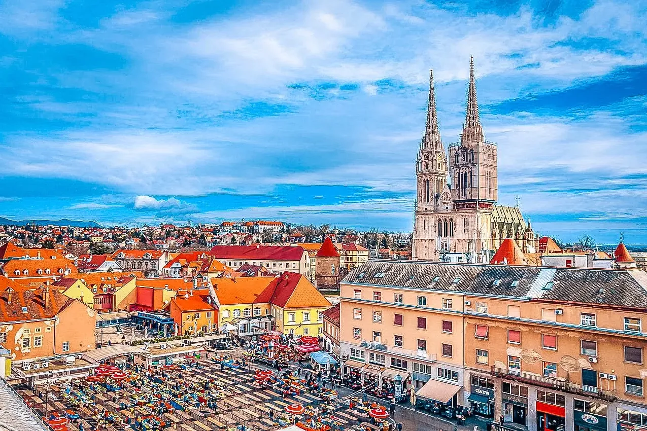 Aerial view of Zagreb with the Cathedral featuring two spires, partially scaffolded, and a bustling outdoor market with re...