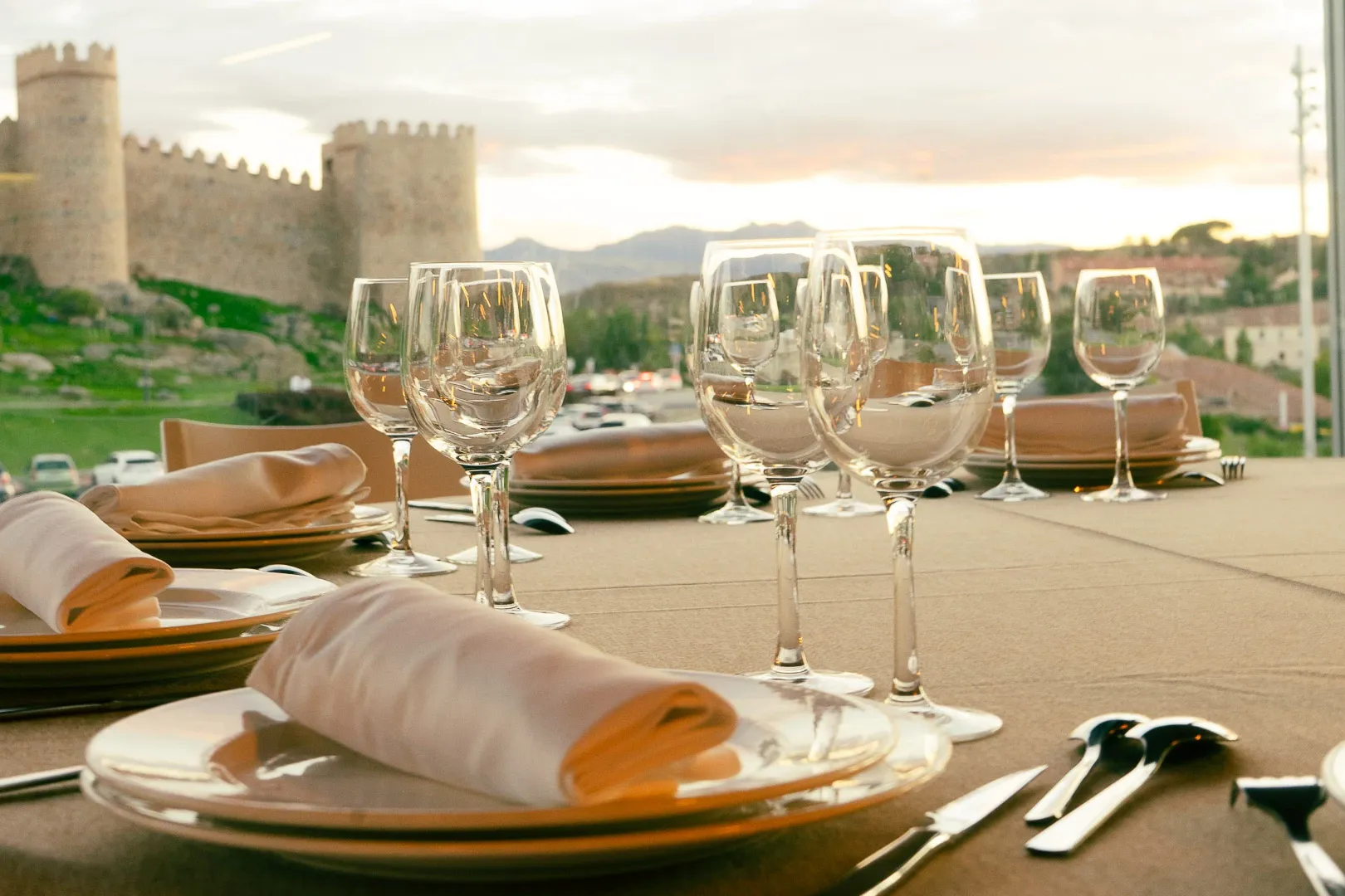 A dining table set with glasses and plates, overlooking the medieval city walls of Ávila, Spain at sunset.