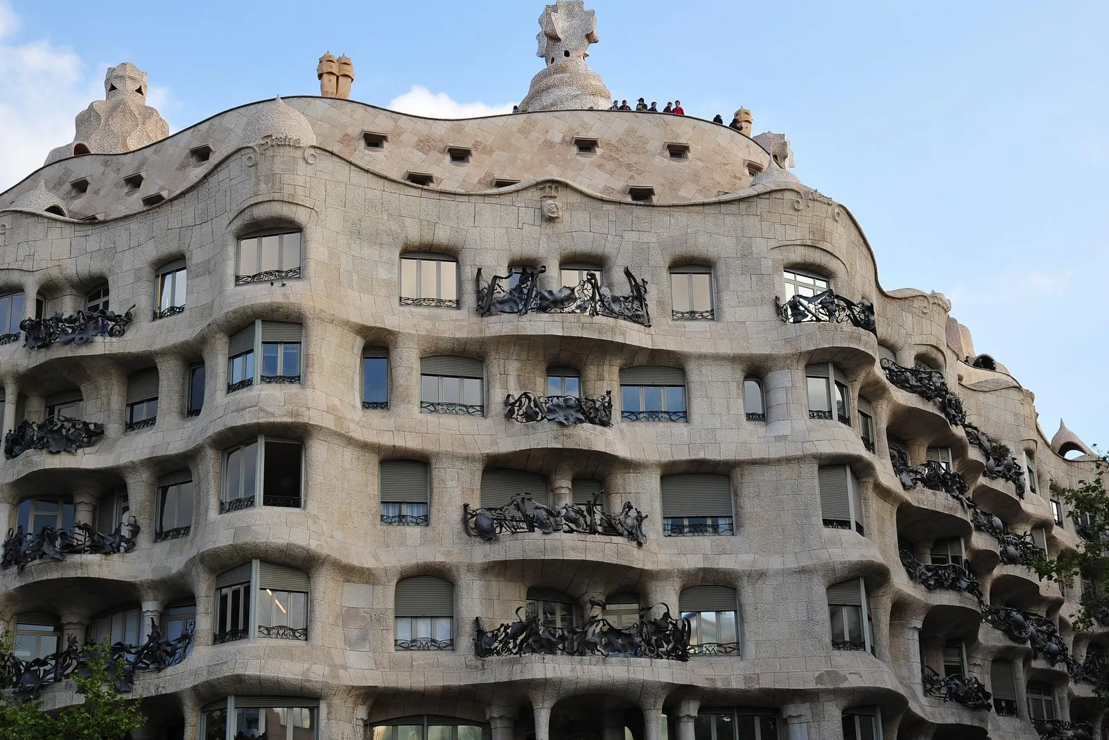 Curved stone facade of Casa Milà (La Pedrera) with ornate iron balconies under a blue sky, designed by Antoni Gaudí.