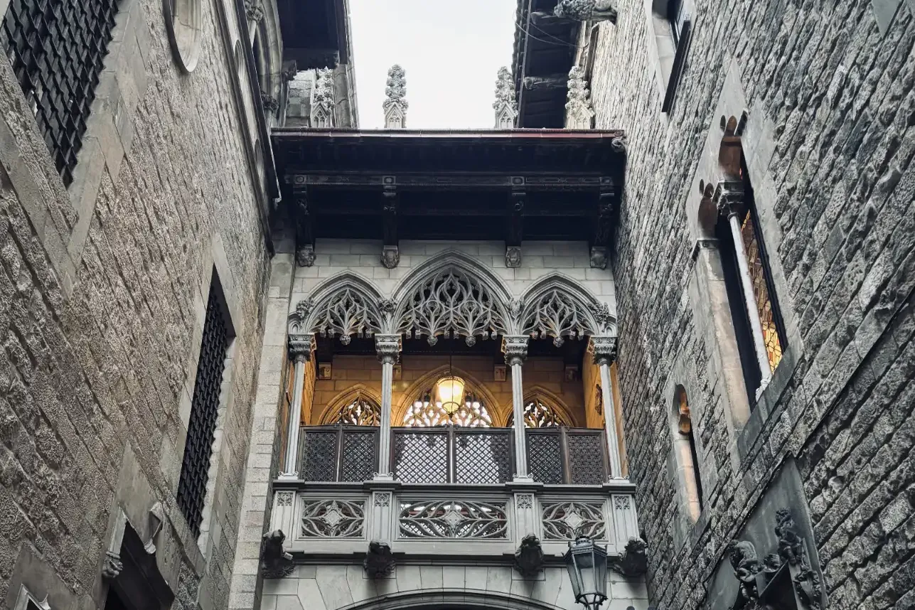 Ornate stone neo-Gothic bridge with a lantern and archway connecting two medieval-style buildings in a narrow alley.