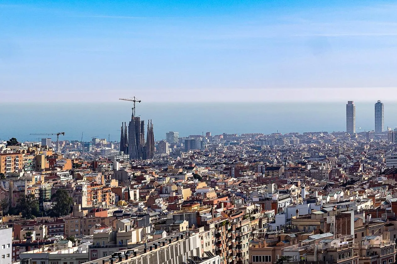 Panoramic view of Barcelona city with Sagrada Familia under construction, Agbar Tower, and two skyscrapers by the sea.